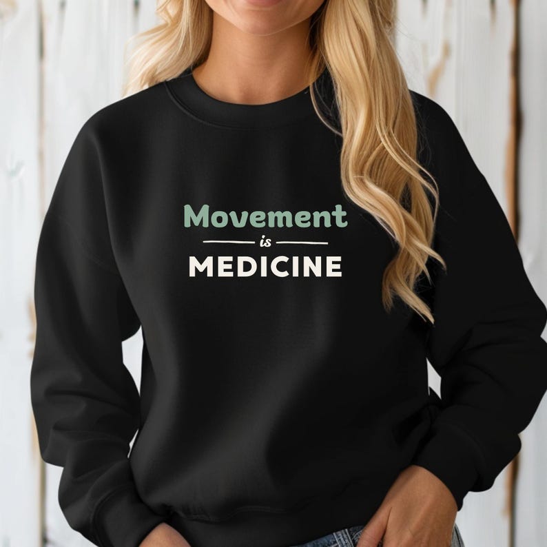May include: Black sweatshirt with the text "Movement is Medicine" in white and light green. The sweatshirt is a crew neck style. The text is centered on the chest.