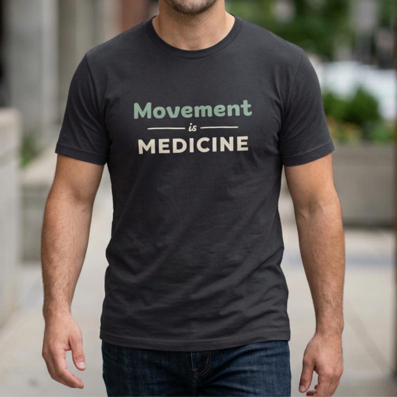 May include: Dark gray t-shirt with the text "Movement is Medicine" in green and white. The shirt has a crew neck and short sleeves. The shirt is made of a soft material.