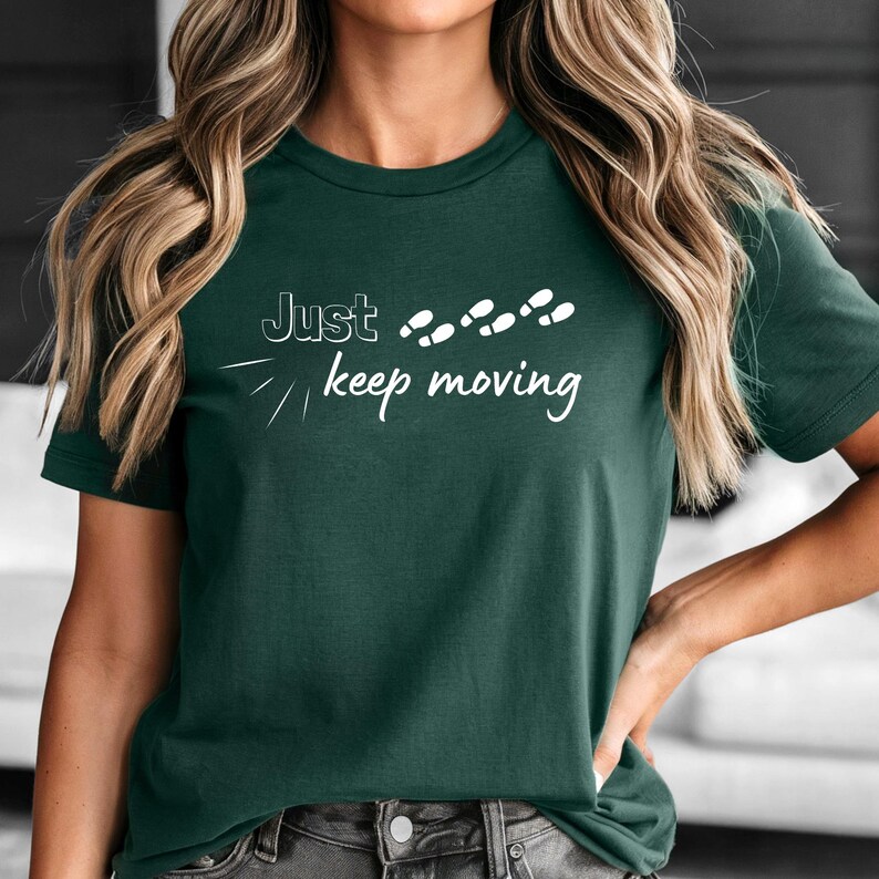 Peut inclure: T-shirt vert fonc&eacute; avec l'inscription blanche &laquo;&nbsp;Just keep moving&nbsp;&raquo; et des empreintes de pas blanches. Le t-shirt est de style col rond.