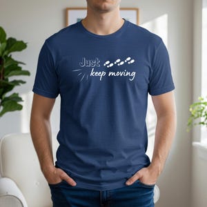 Peut inclure: T-shirt bleu marine avec l'inscription blanche "Just keep moving" et des empreintes de pas blanches. Le t-shirt est en mati&egrave;re douce, id&eacute;al pour un usage d&eacute;contract&eacute;. Design simple et motivant.