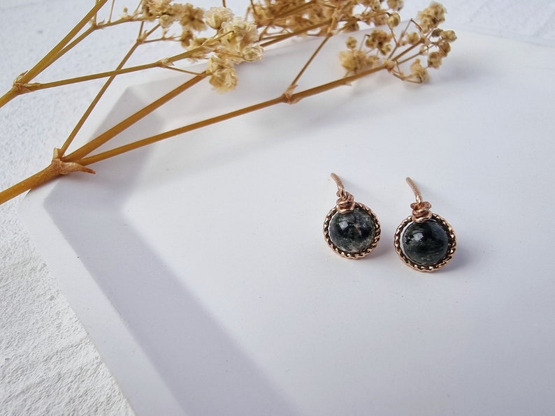 May include: A pair of earrings with black and white stone accents and a rose gold wire frame.