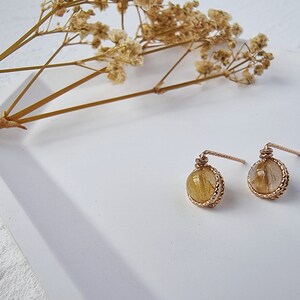 May include: A pair of gold earrings with small round stones. The stones are a light brown color with gold flecks.