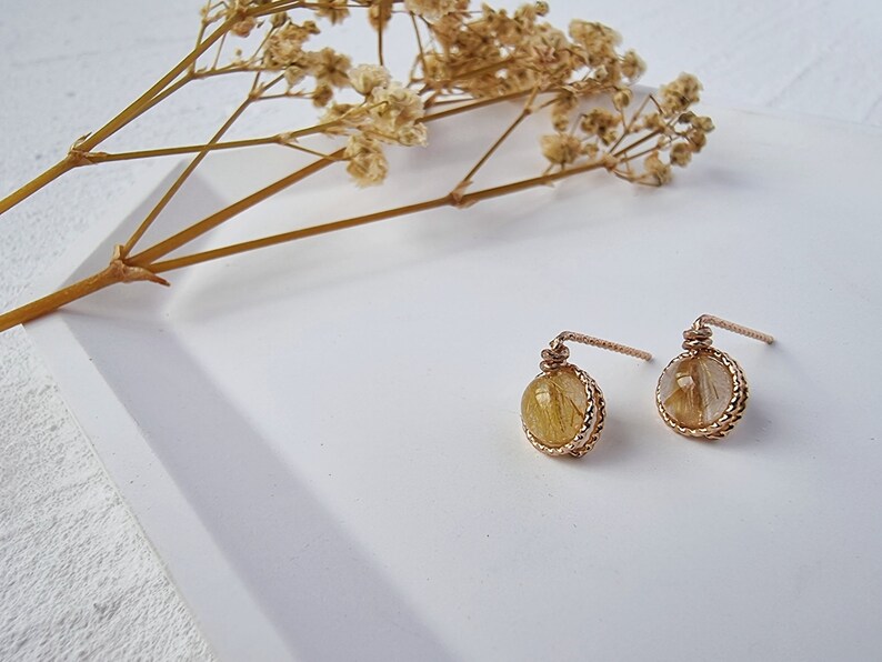 May include: A pair of gold earrings with small round stones. The stones are a light brown color with gold flecks.