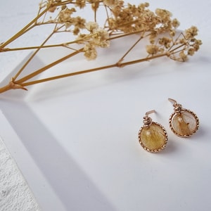 May include: A pair of gold earrings with a delicate wire design and a round, clear stone with yellow and brown inclusions.