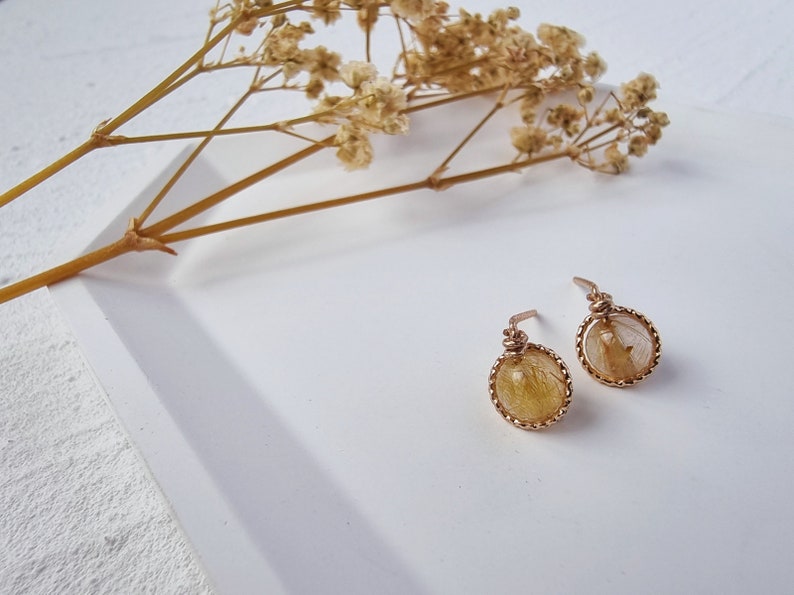 May include: A pair of gold earrings with a delicate wire design and a round, clear stone with yellow and brown inclusions.