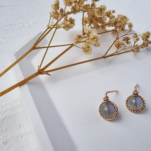 May include: A pair of silver earrings with a round, iridescent labradorite stone set in a gold-toned bezel. The earrings have a delicate, wire-wrapped design.