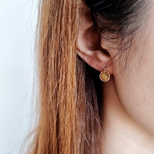 May include: A close-up of a person's ear with a small gold earring. The earring is round and has a textured surface.