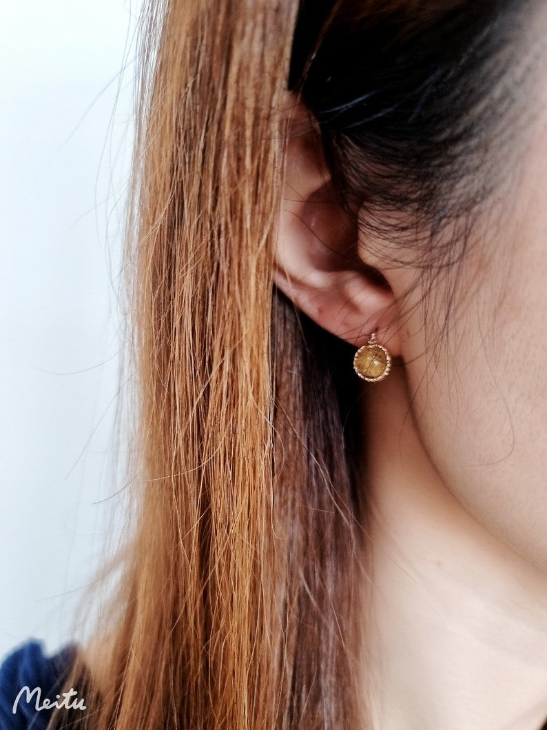 May include: A close-up of a person's ear with a small gold earring. The earring is round and has a textured surface.