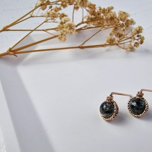 May include: A pair of gold earrings with black and green stone accents. The earrings are on a white surface.