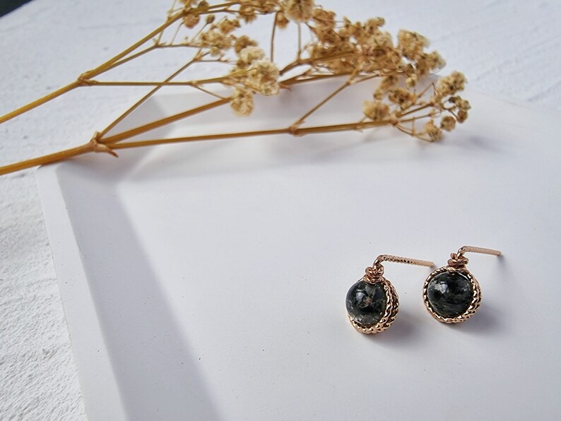 May include: A pair of gold earrings with black and green stone accents. The earrings are on a white surface.