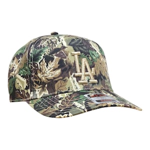 May include: A camouflage baseball cap with the letters "LA" embroidered on the front. The cap has a curved peak and a classic six-panel design. The hat is made of a durable fabric and has a structured fit.