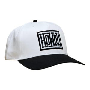 Può includere: Un cappellino da baseball bianco con visiera nera e un bottone nero sulla parte superiore. La parte anteriore presenta una toppa rettangolare nera con la parola HOWDY ricamata in lettere bianche, circondata da un bordo nero e cuciture bianche.