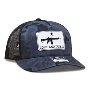 May include: A navy blue camouflage baseball cap with a black mesh back. The front features a white rectangle with a black rifle graphic and the text "COME AND TAKE IT".