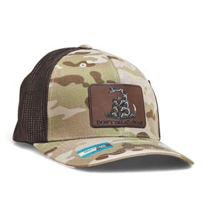 May include: A camouflage baseball cap with a brown mesh back and a curved brim. The front features a brown leather patch with a coiled snake and the text "DON'T TREAD ON ME". The brim has a "MultiCam" label.