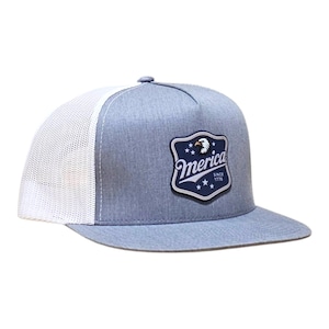 Op de afbeelding: Een baseballpet in gemêleerd blauw met een witte mesh achterkant en een platte klep. De voorkant heeft een donkerblauwe, schildvormige patch met een adelaar, de tekst 'merica', 'SINCE 1776' en drie witte sterren onder de belettering.