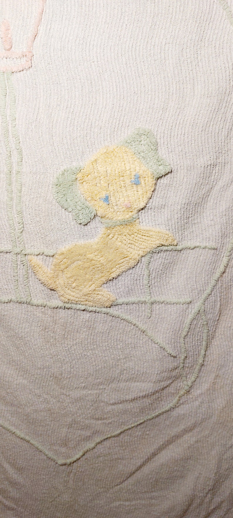May include: A white crocheted baby blanket with a yellow puppy design. The puppy has blue eyes and a pink nose.
