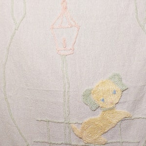 May include: A white crocheted baby blanket with a light pink lamppost and a yellow dog embroidered on it.