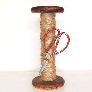 May include: A wooden spool wrapped in natural twine with a pair of red and silver scissors tucked into the twine.