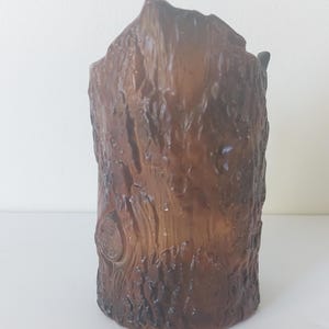 May include: A brown ceramic vase shaped like a tree trunk. The vase has a rough, textured surface that resembles bark.
