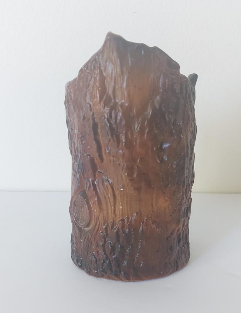 May include: A brown ceramic vase shaped like a tree trunk. The vase has a rough, textured surface that resembles bark.