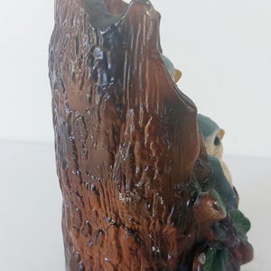 May include: A ceramic figurine of two bluebirds perched on a tree stump. The stump is brown and has a rough texture. The birds are painted in shades of blue and white.