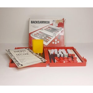 May include: A vintage backgammon game set with a red case, dice, and game pieces. The box reads "BACKGAMMON by Guilded". The game pieces are red, white, and black. A yellow plastic cup is also included.