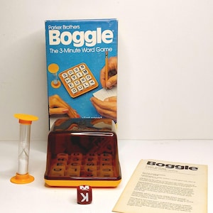 May include: Vintage Boggle word game by Parker Brothers. The game includes a brown and yellow plastic grid with lettered dice, a red die with the letters M and K, an hourglass timer, and the game box with the text "Boggle The 3-Minute Word Game".