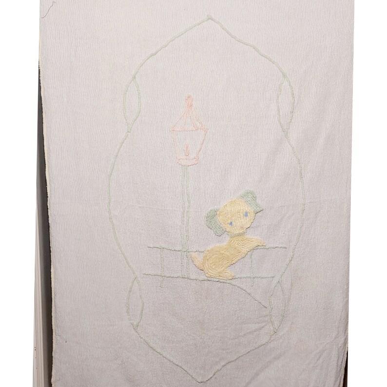 May include: A white embroidered baby blanket with a light green border and a yellow dog with blue eyes sitting under a pink and green lamppost.