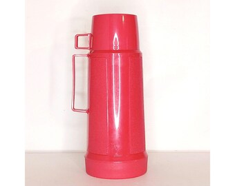 May include: A bright pink thermos with a handle and a lid. The thermos has a textured surface.