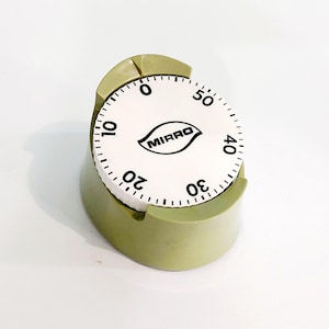 May include: A vintage kitchen timer with a white dial and black numerals, marked from 0 to 50. The timer has a green base and the brand name "MIRRO" is printed on the dial. The timer is designed to sit upright.