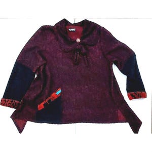 May include: A burgundy-colored sweater with a dark blue sleeve and a red and black patterned cuff. The sweater has a round collar, a decorative button, and a small pocket with a turquoise accent.