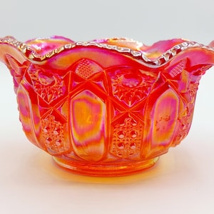 May include: A vibrant, iridescent glass bowl with a ruffled rim. The bowl features a detailed, textured pattern in shades of red, orange, and pink. The decorative bowl has a round base and is likely used for serving.