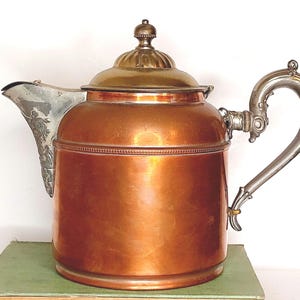 May include: A copper teapot with a silver lid and handle. The teapot has a decorative design on the spout and handle.