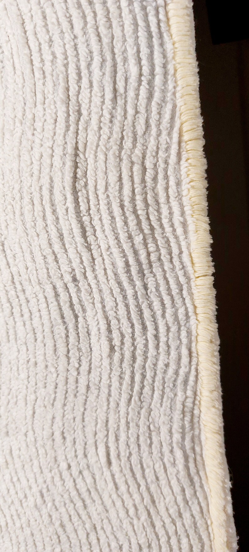 May include: White bath rug with a textured, wavy pattern and a cream-colored fringe border.