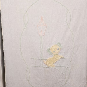 May include: A white baby blanket with a light green embroidered design of a dog sitting under a lamppost. The dog is yellow with blue eyes and the lamppost is pink.