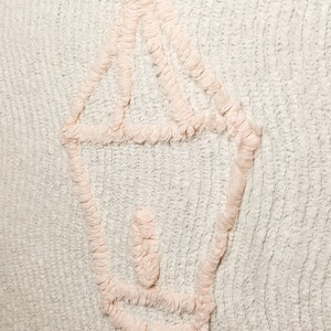 May include: A white textured fabric with a pink embroidered design of a lantern. The lantern has a rounded top and a long stem.