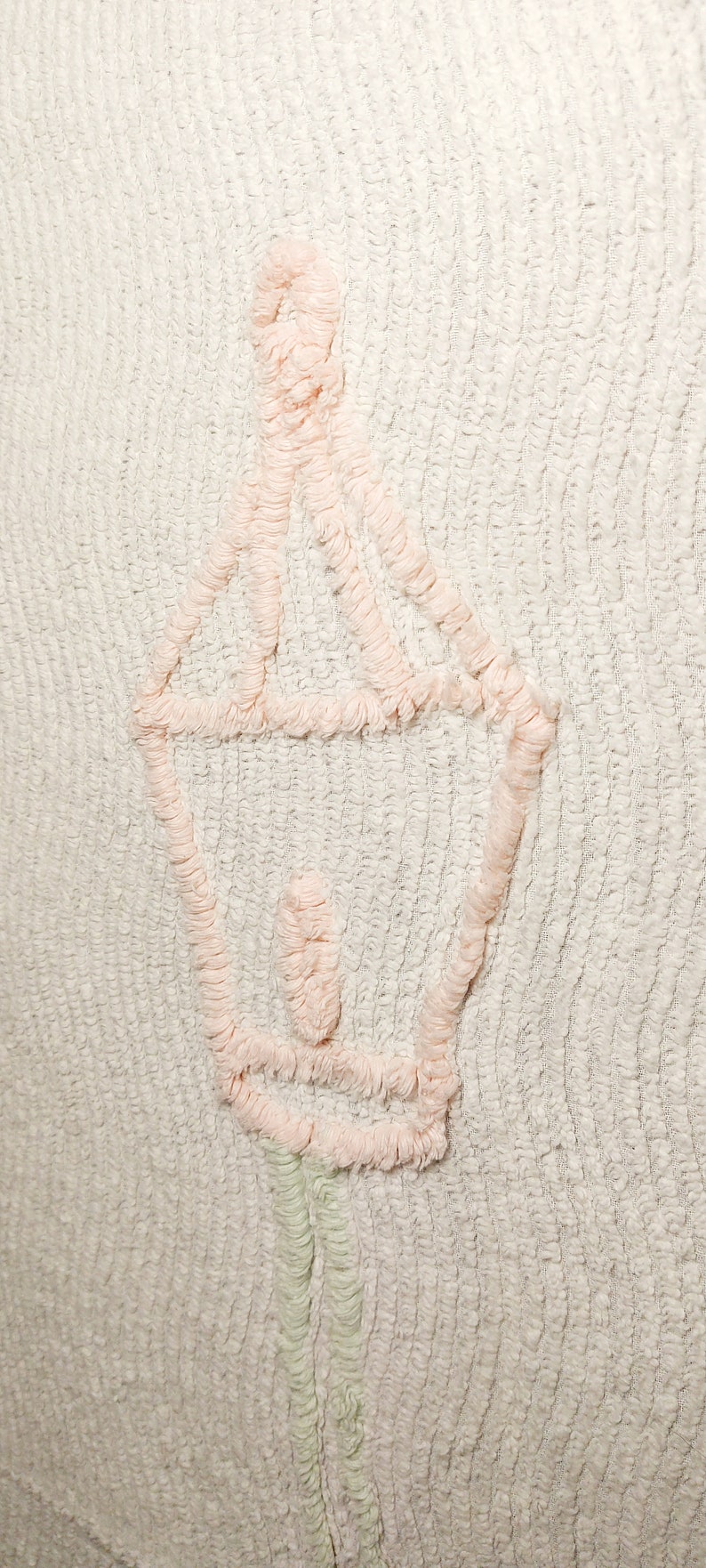 May include: A white textured fabric with a pink embroidered design of a lantern. The lantern has a rounded top and a long stem.
