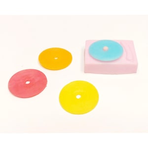 May include: A pink miniature record player with a light blue record on top. Three colorful records in red, yellow, and orange are scattered around the record player. The records have a hole in the center.