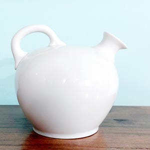 May include: A white ceramic pitcher with a rounded body and a spout. The pitcher has a handle and a smooth, glossy finish.