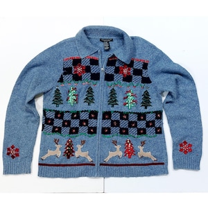 May include: A light blue zip-up sweater with Christmas-themed embroidery. The sweater features a checkered pattern with red and green accents, embroidered Christmas trees, reindeer, and snowflakes. The sweater has a collared neckline and ribbed cuffs.