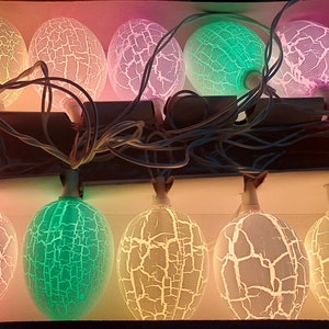 May include: A string of 10 LED light bulbs with a cracked glass design. The bulbs are in a variety of colors, including pink, green, and white.