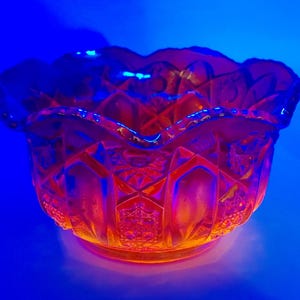 May include: An orange glass bowl with a scalloped rim and geometric patterns. The bowl is illuminated with blue and orange light, creating a vibrant and colorful display. The bowl is likely vintage or antique.