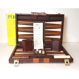May include: A vintage backgammon set in a brown leather case with a handle. The game board features a white, brown, and tan design. Includes dice, dice cups, and game pieces. A yellow box is visible in the background.