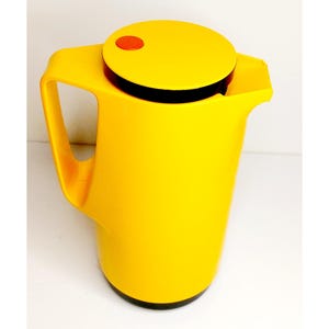 May include: A yellow thermal carafe with a black lid and a red button on top. The carafe has a handle and a spout.