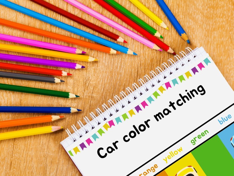 May include: A notebook with the title "Car color matching" and a color chart with the colors orange, yellow, green, and blue. There are colored pencils in a rainbow of colors on a wooden surface.