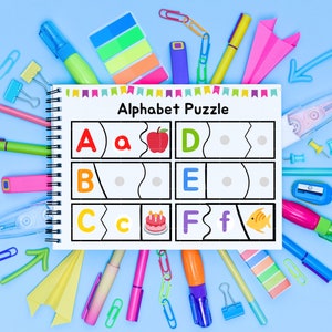 May include: A white alphabet puzzle with colorful illustrations of an apple, birthday cake, and fish. The puzzle is surrounded by colorful school supplies, including markers, paper clips, push pins, and sticky notes.