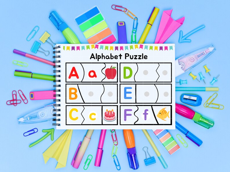May include: A white alphabet puzzle with colorful illustrations of an apple, birthday cake, and fish. The puzzle is surrounded by colorful school supplies, including markers, paper clips, push pins, and sticky notes.