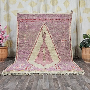 May include: A pink and cream Moroccan rug with a geometric pattern. The rug has a fringe border and is displayed on a wooden floor.