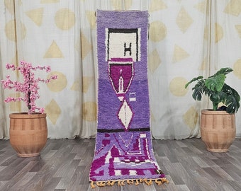 May include: A rectangular, purple and white patterned rug with a geometric design. The rug features a central design with a white diamond shape and black accents. The rug has a fringe of yellow tassels at the bottom.