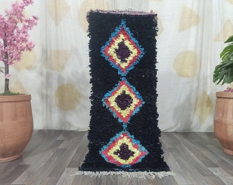 May include: A black and white Moroccan rug with colorful diamond patterns. The rug has a fringe border and is made of wool.